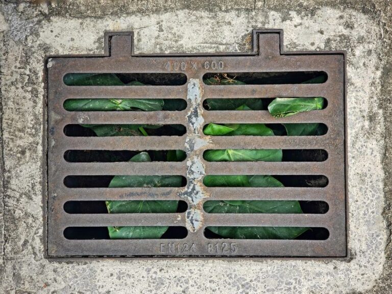 Workers inspect heavy-duty trench drain grates installed in concrete on a paved commercial driveway.