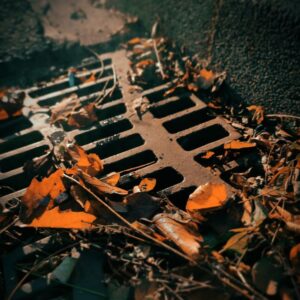 A maintenance worker inspects a long grated trench drain installed in an outdoor commercial parking lot.