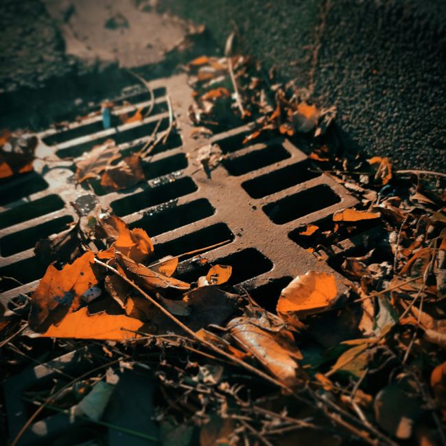 A maintenance worker inspects a long grated trench drain installed in an outdoor commercial parking lot.