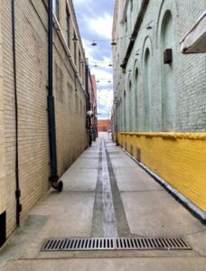 Heavy-duty trench drain with metal grate across a concrete loading dock beside parked freight trailers.