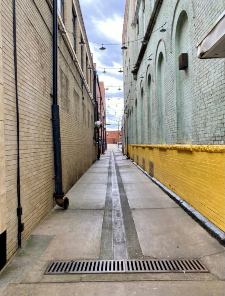 Heavy-duty trench drain with metal grate across a concrete loading dock beside parked freight trailers.