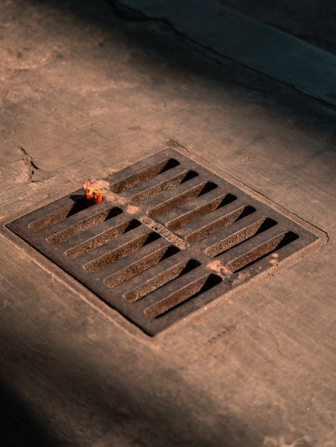 Two workers in safety gear installing heavy metal trench drain grates in a commercial parking lot.