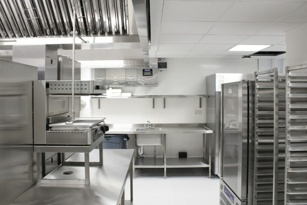 Commercial kitchen workers review a floor drainage layout beside an installed trench drain and stainless steel grating.